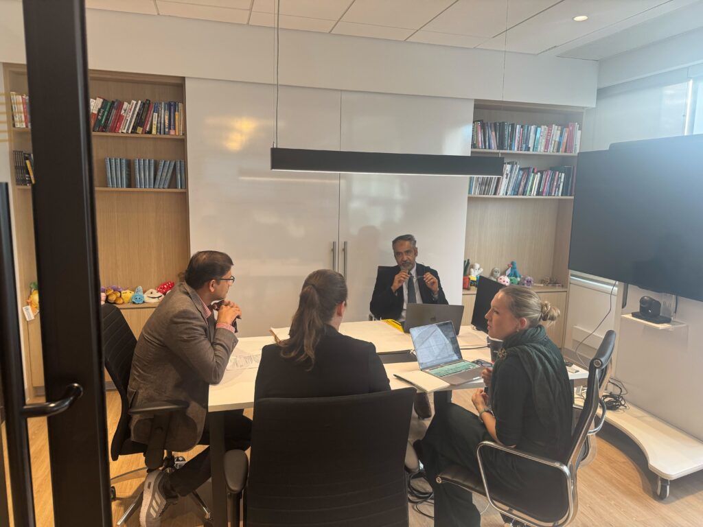 Workshop attendees seated and standing around a table, actively engaged in discussion during the Integrated One Health Research and Policy Workshop: Bridging Sectors and Disciplines.