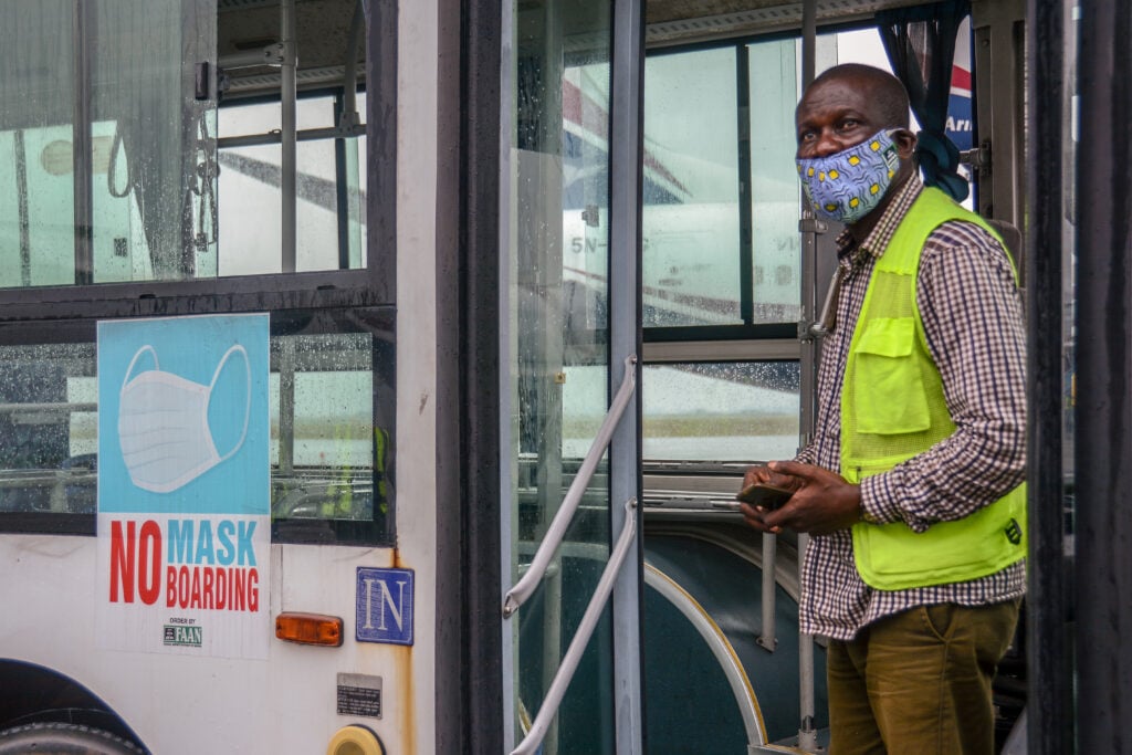 A staff at the Lagos airport stands at the door of a bus which reads "No Mask No Boarding" as domestic flights resume in Nigeria, July 8, 2020.