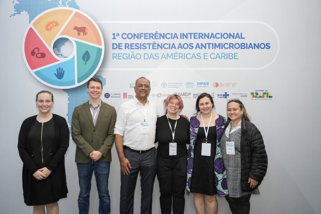 Global Strategy Lab team members and André Abreu stand together for a group photo in front of the conference backdrop at the 1st Americas Regional Meeting on Antimicrobial Resistance in Brasília.